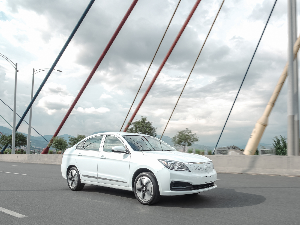 Sedán eléctrico Dongfeng E70 visto en ángulo frontal, con faros estilizados, parrilla cerrada y sombra proyectada sobre el suelo.