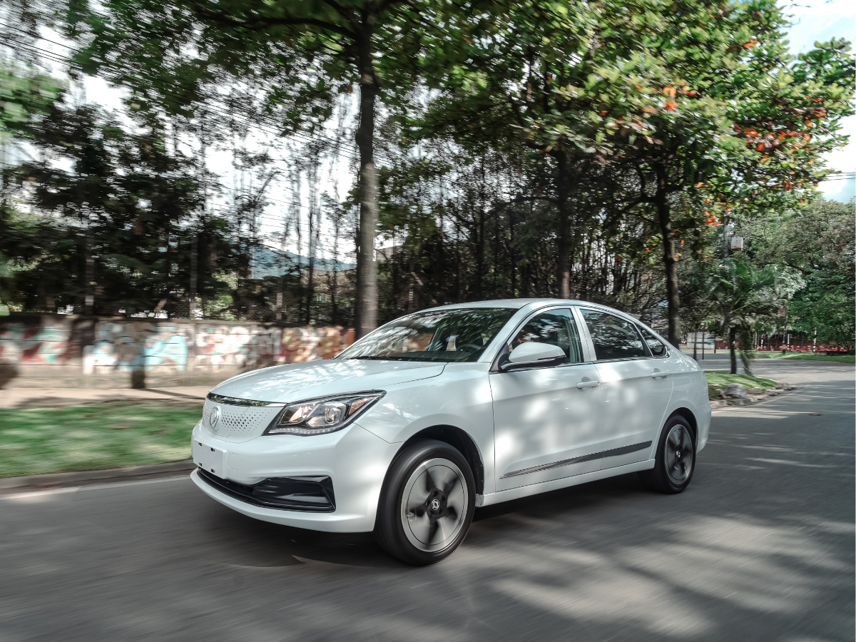 Sedán eléctrico Dongfeng E70 de diseño moderno, estacionado sobre superficie urbana con iluminación natural.